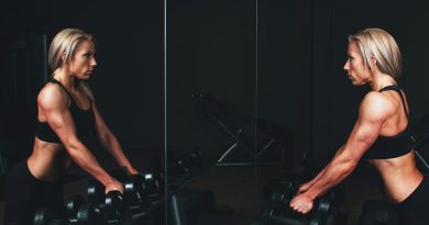 woman wearing black top top holding black dumbbells standing in front of mirror