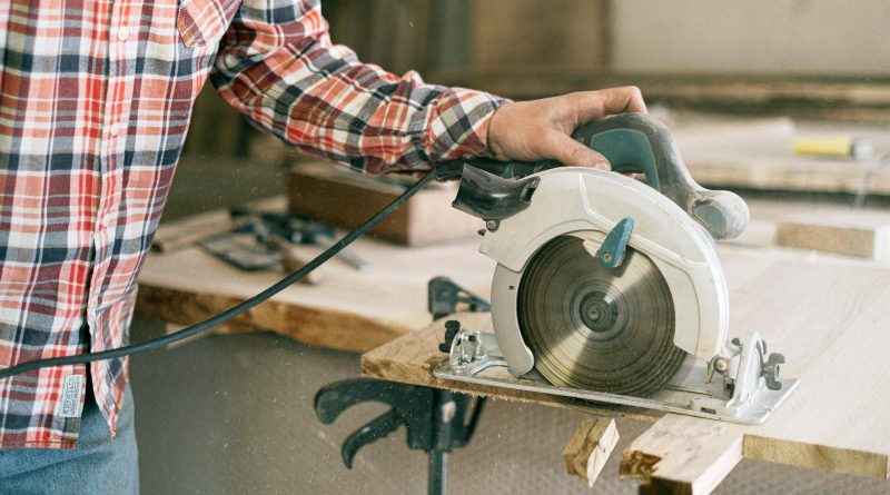 A carpenter in a plaid shirt uses a circular saw in a workshop, showcasing craftsmanship.