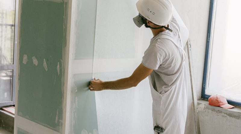 Construction worker in hard hat applying wallpaper inside a building under renovation.