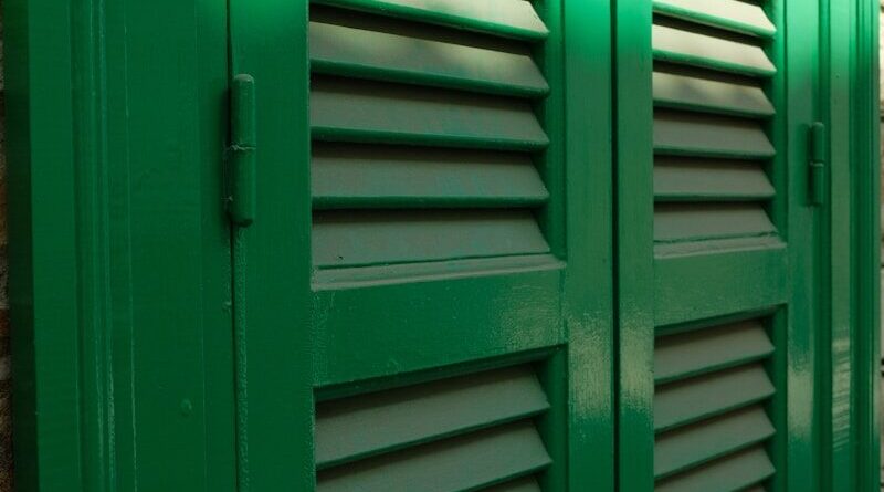 Green louvered shutters on a brick wall.